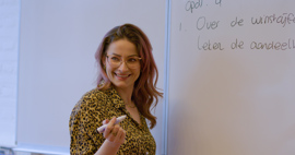 A teacher stands in front of the classroom with a pen and wants to write something on a whiteboard.